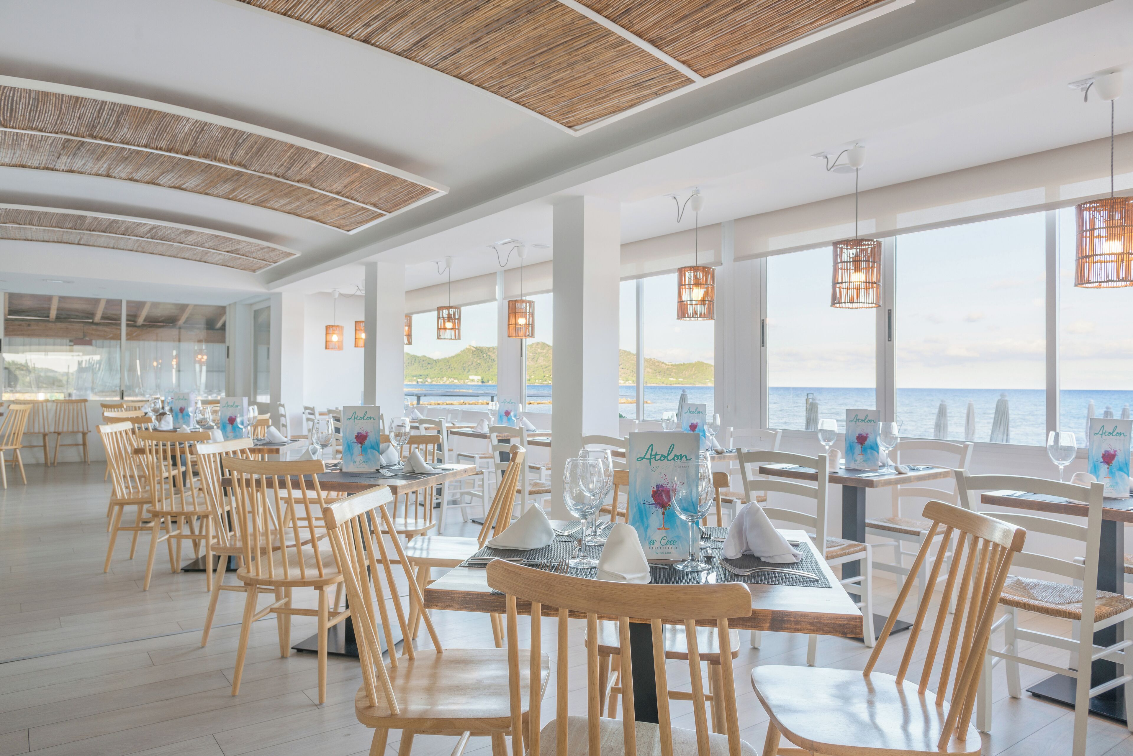 A restaurant with wooden chairs and tables, large windows, and hanging light fixtures.