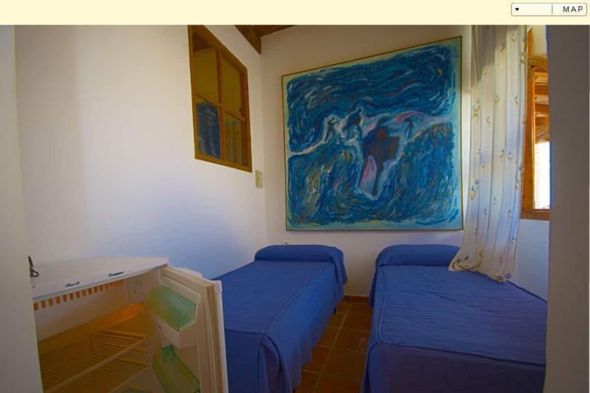 Una habitación con dos camas, un cuadro en la pared y una mesita con una silla.