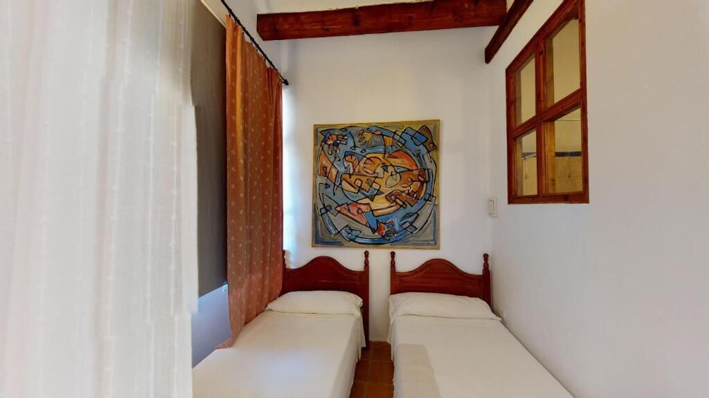 A room with two beds, a painting on the wall, and a window with wooden frames.