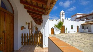A courtyard with a white building, a wooden door, and a stone floor.