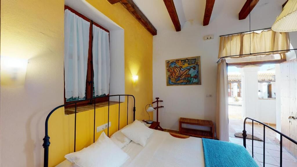Un dormitorio con cama, ventana con cortinas, un cuadro en la pared y un banco.