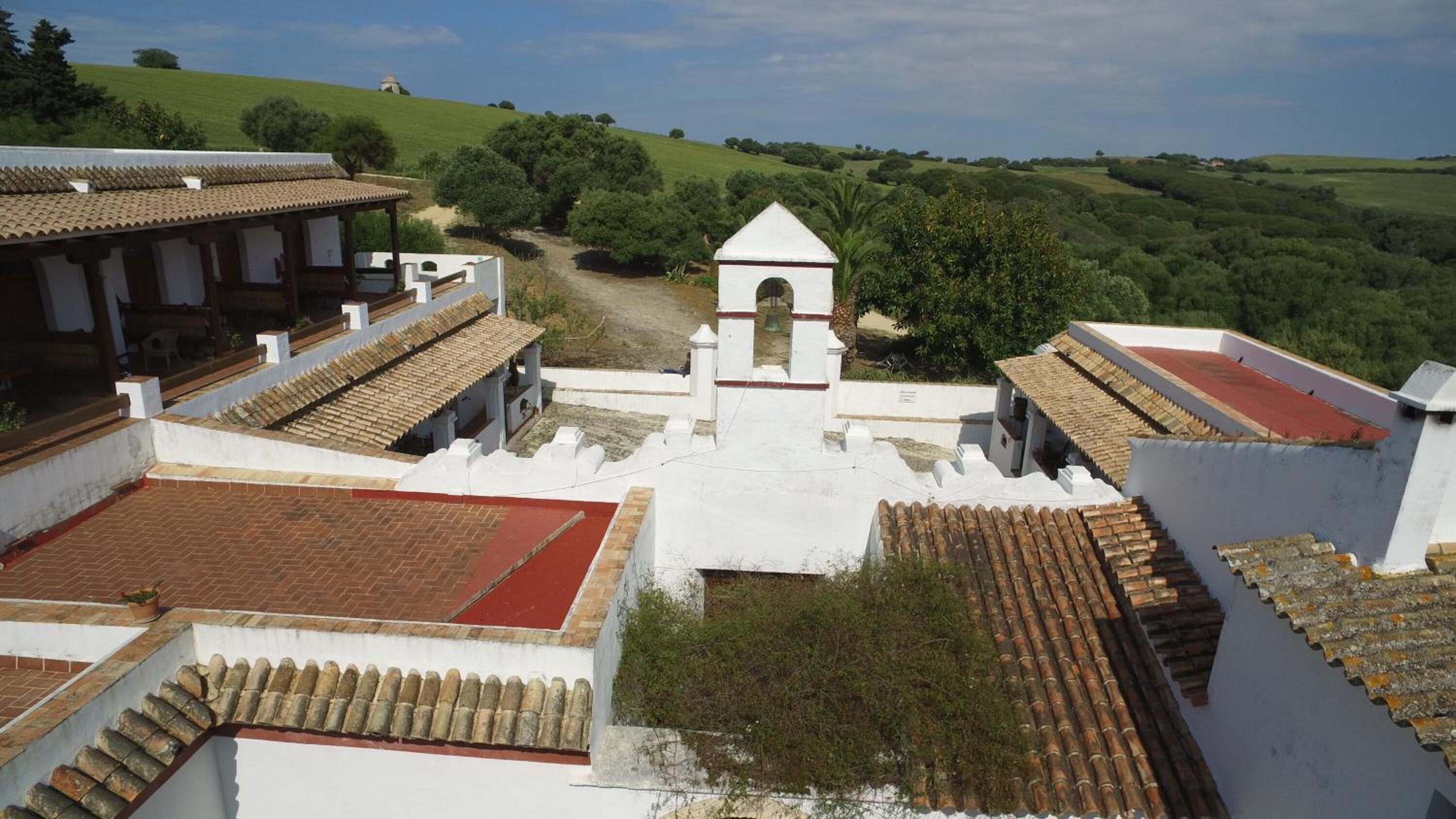 A view of a courtyard with white buildings, a central tower, and surrounding greenery.