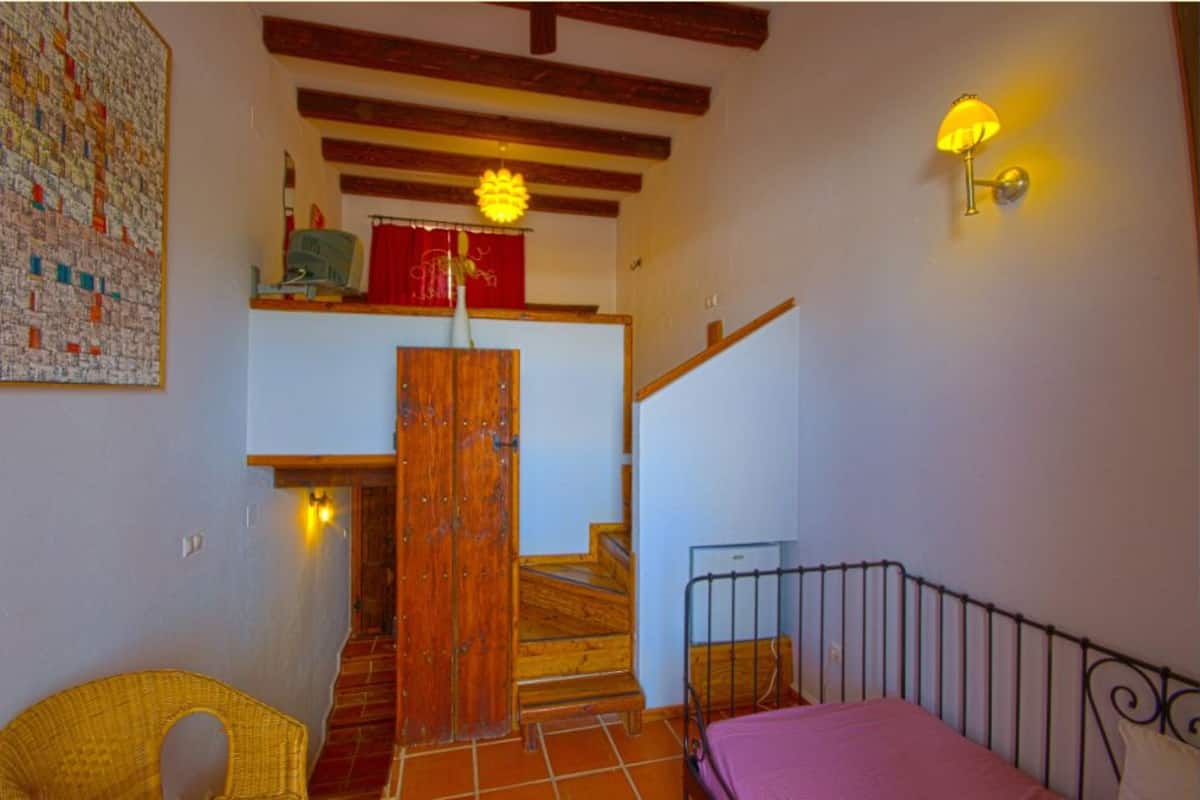 Un dormitorio con cama, una escalera de madera, una lámpara de pared y un adorno en la pared.