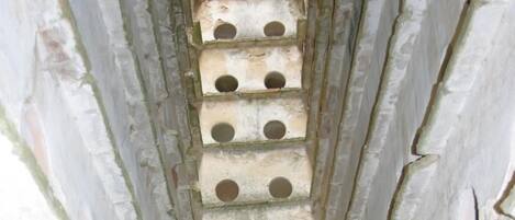 Um corredor de pedra estreito, com aberturas circulares e uma porta no final.