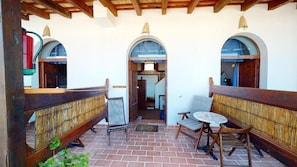 A covered outdoor area with a wooden bench, a small table, and a chair. There are arched doorways and a tiled floor. - El Palomar de la Breña (Barbate)