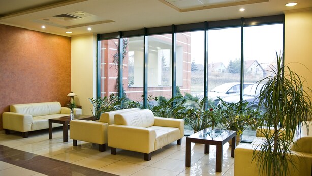 Un vestíbulo de hotel con zona de estar, ventanas amplias y plantas de interior.