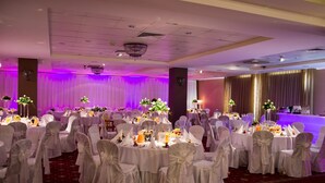 Un salón de banquetes con mesas redondas, manteles blancos y sillas con cintas blancas.