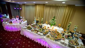 Montaje de bufé con varias mesas cubiertas con manteles blancos, mostrando una variedad de alimentos y decoración floral.
