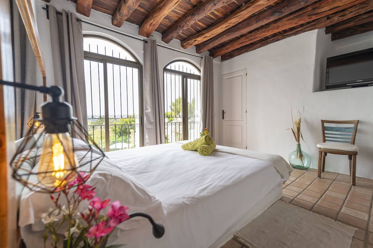 Una camera da letto con un letto grande, un soffitto in legno, una TV a parete e una finestra con tende.