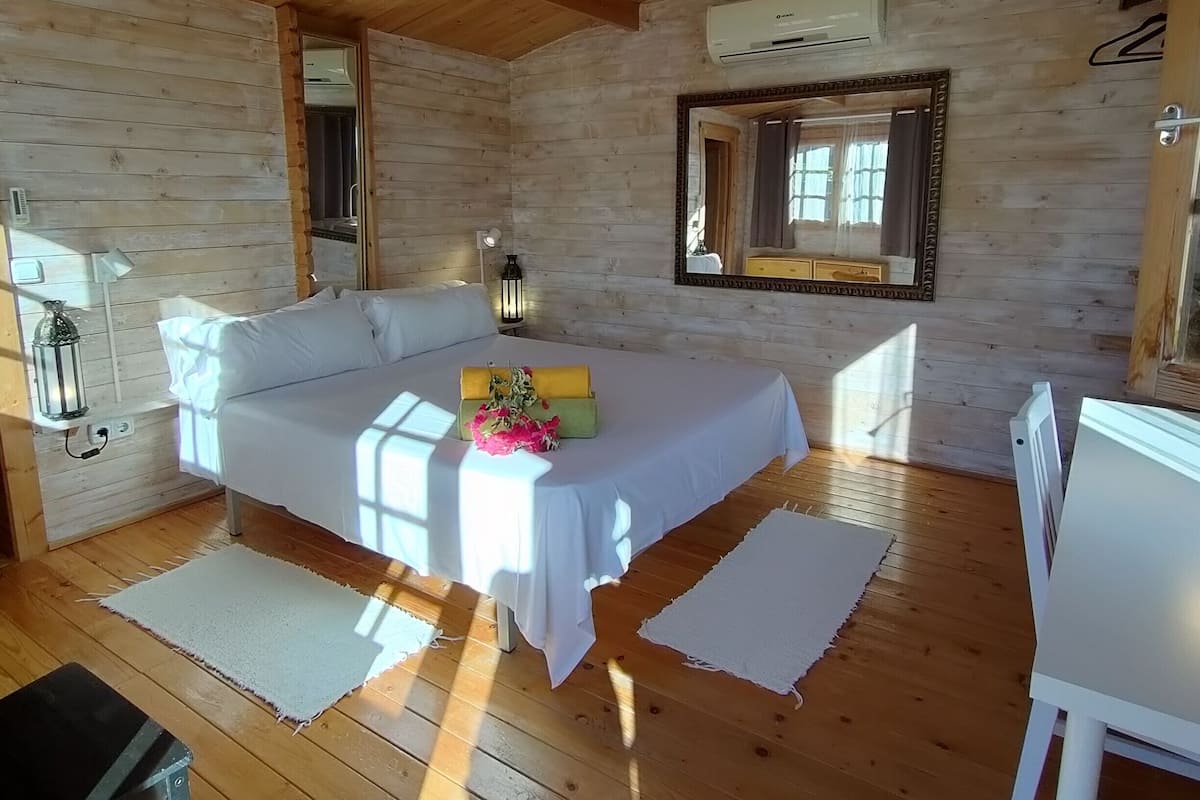 Accogliente camera da letto in legno con un letto, lampade da comodino, uno specchio e un piccolo tavolo.