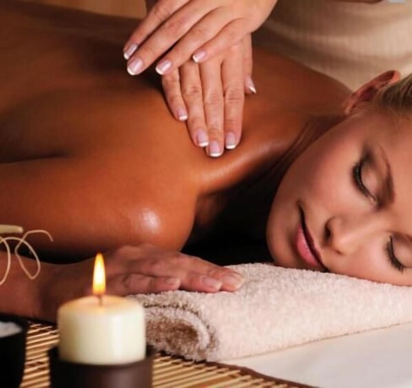 A person receiving a massage with a candle on a table.