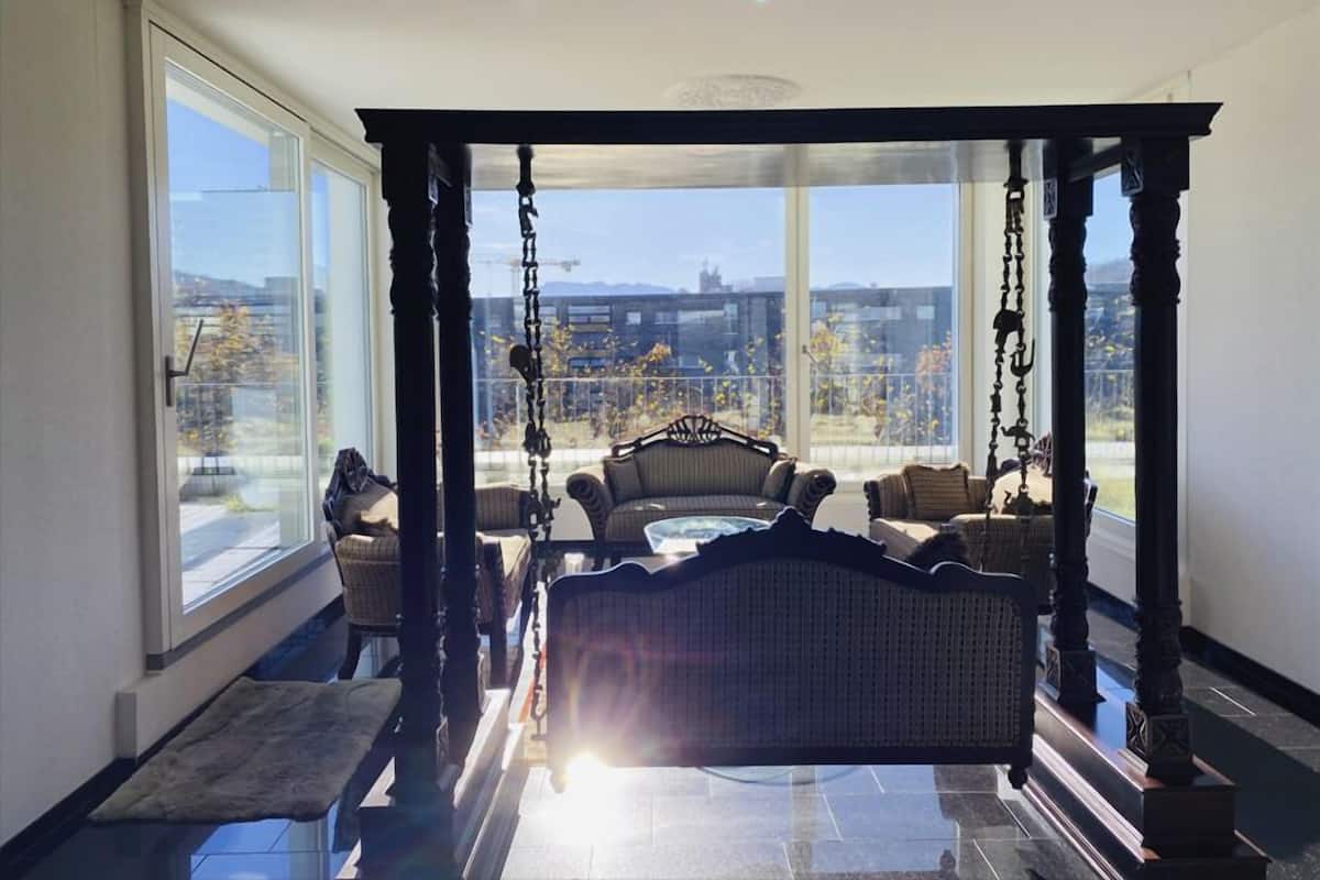 Una habitación soleada con una silla colgante, ventanas amplias y vistas a un paisaje urbano.