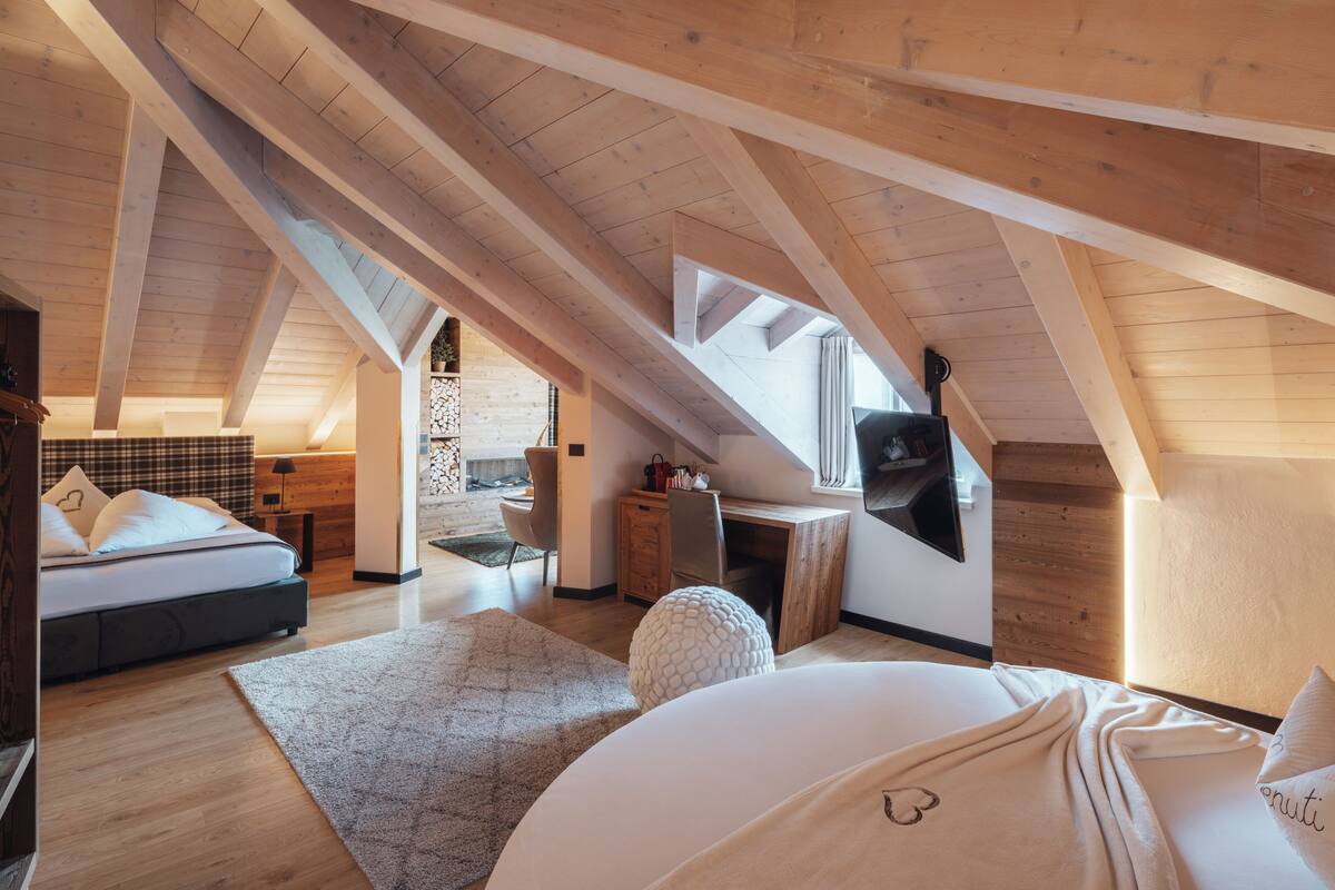 A bedroom with a sloped ceiling, a bed, a desk, and a TV.