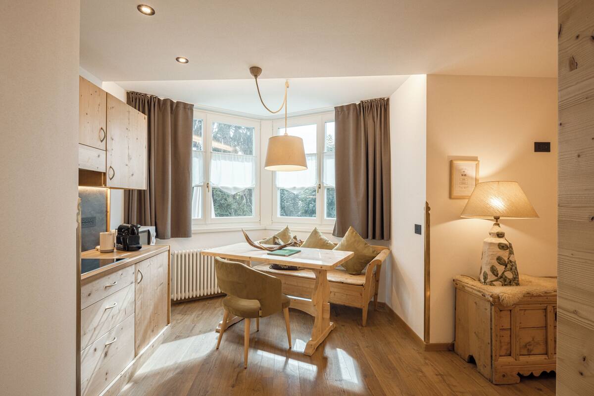 A compact kitchen with a dining table, wooden cabinets, and a window with curtains.