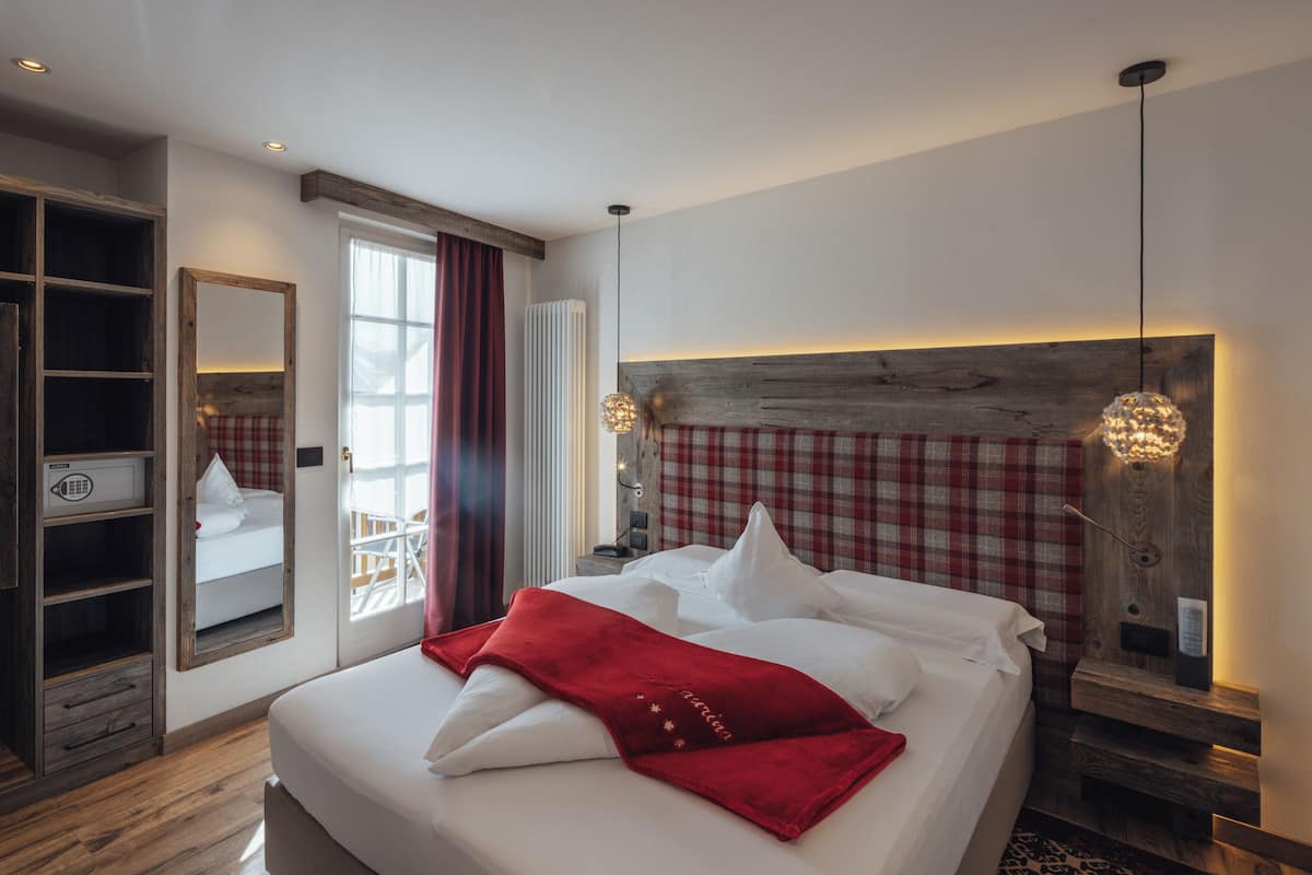 A hotel room with a large bed, a wooden headboard, a wardrobe, and a mirror.