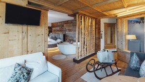 A wooden interior with a sofa, a rocking chair, a bathtub, and a television. - Bio Boutique Hotel Laurino (Cavalese)