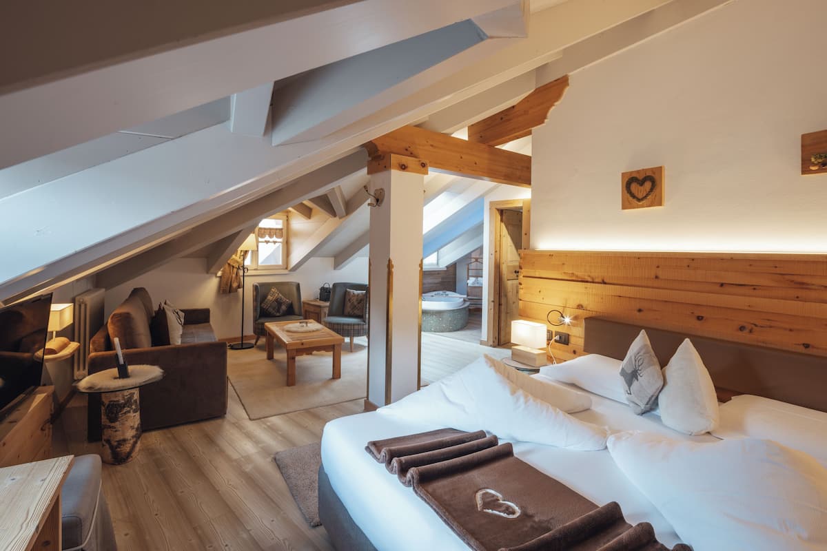 A cozy, well-lit room with a large bed, a wooden ceiling, and a view of a balcony.