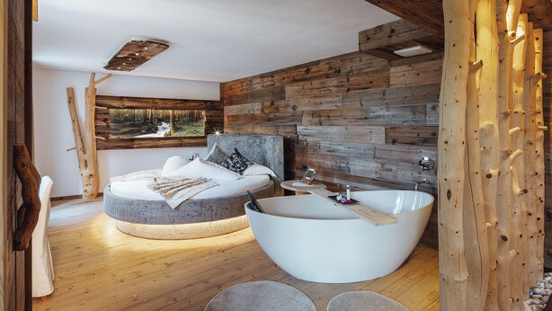 A modern bedroom with a circular bed, a large bathtub, and a wooden wall. - Bio Boutique Hotel Laurino (Cavalese)
