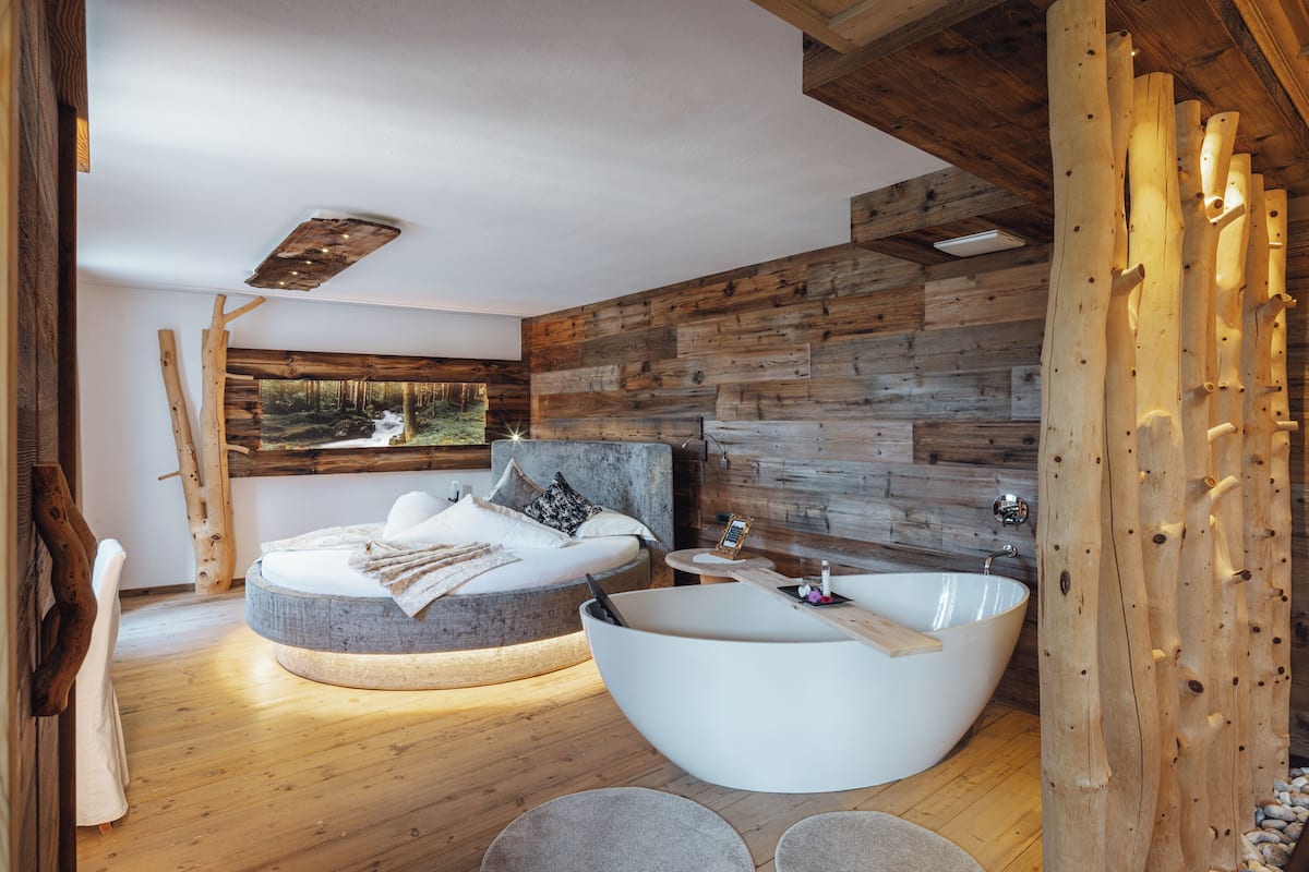 A modern bedroom with a circular bed, a large bathtub, and a wooden wall.