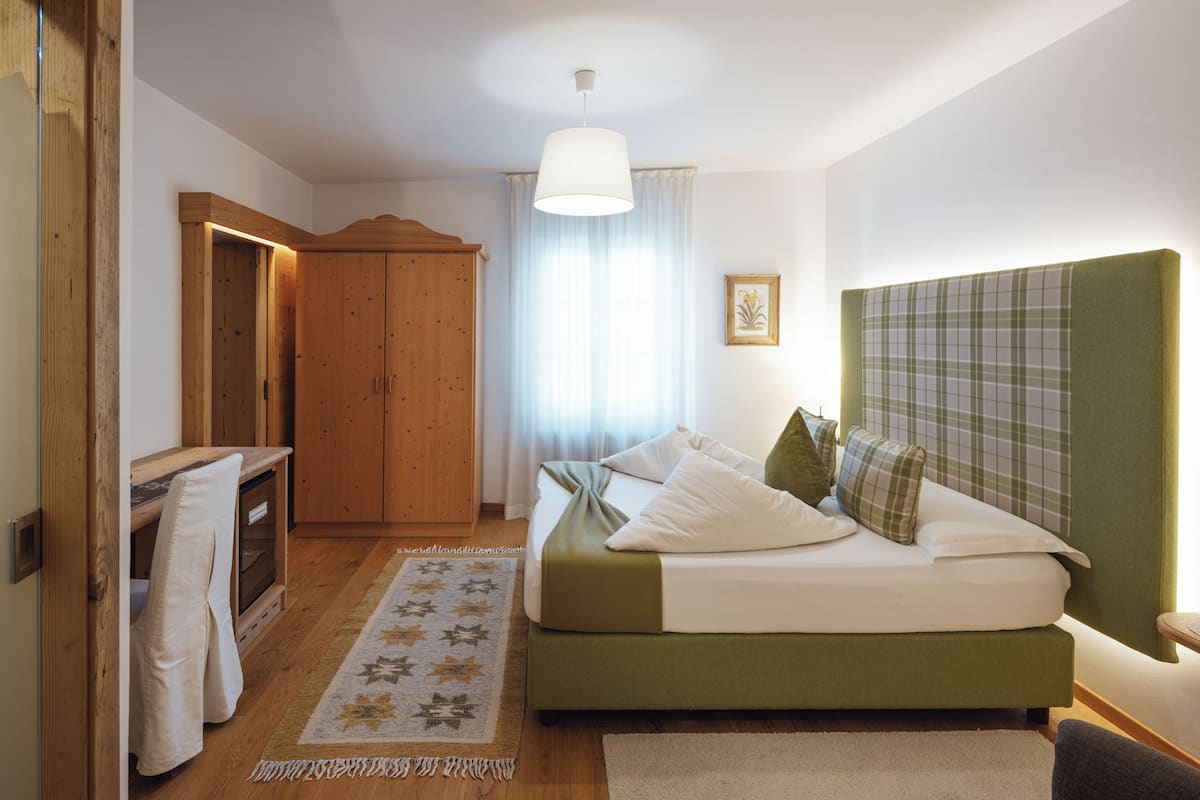 A bedroom with a bed, a wooden wardrobe, a desk, and a window with curtains.