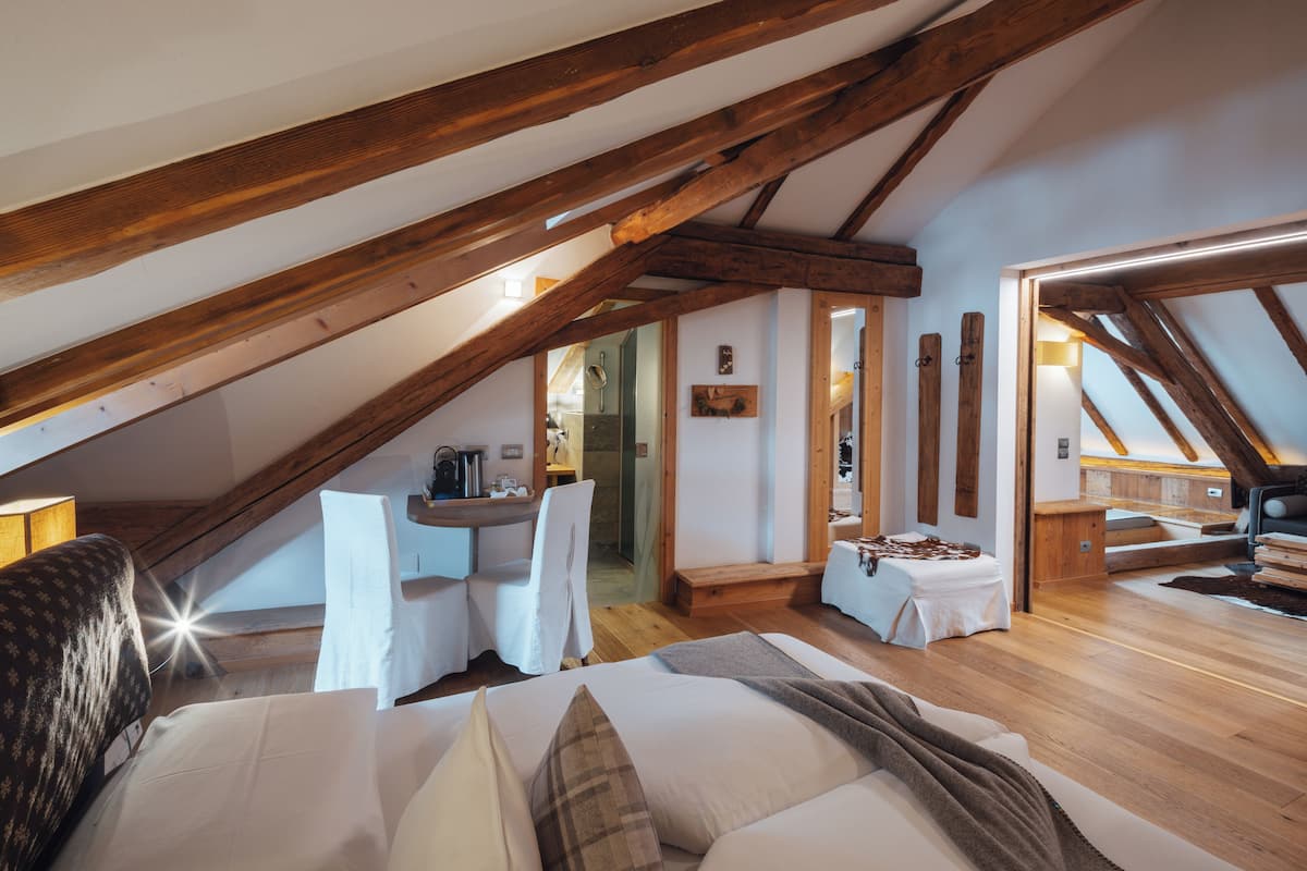 A cozy attic bedroom with exposed wooden beams, a bed, a small desk, and a chair.