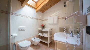 A bathroom with a skylight, a bidet, a toilet, a sink, and a hairdryer.