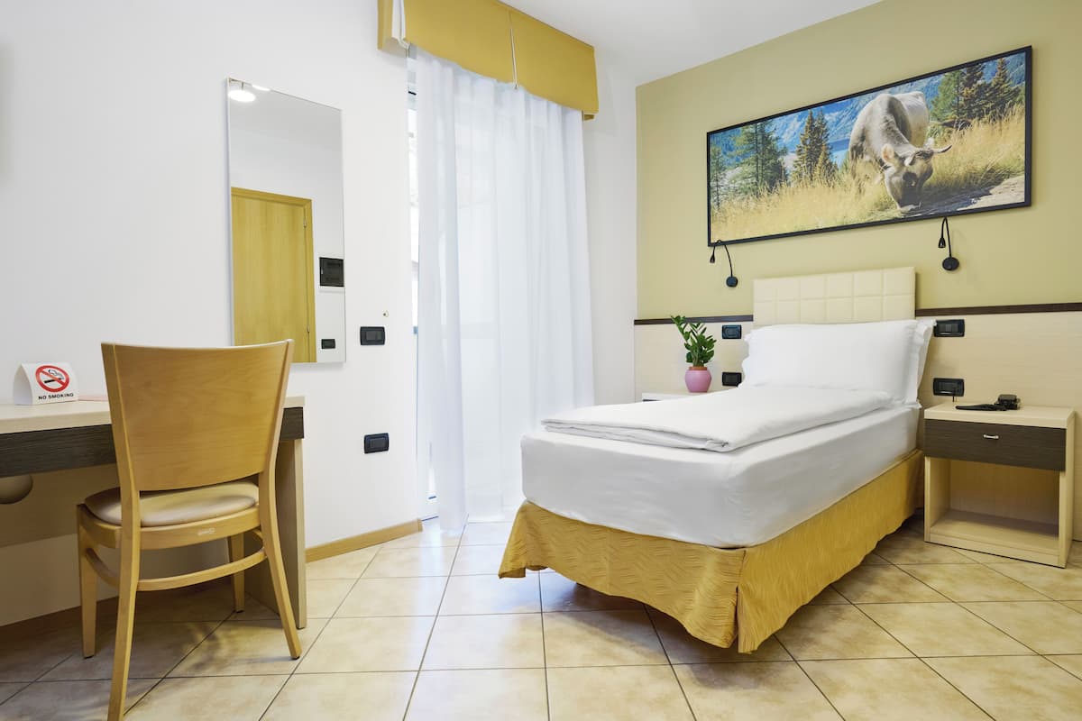 A hotel room with a bed, a chair, a desk, a nightstand, a wall-mounted TV, and a door with a mirror.