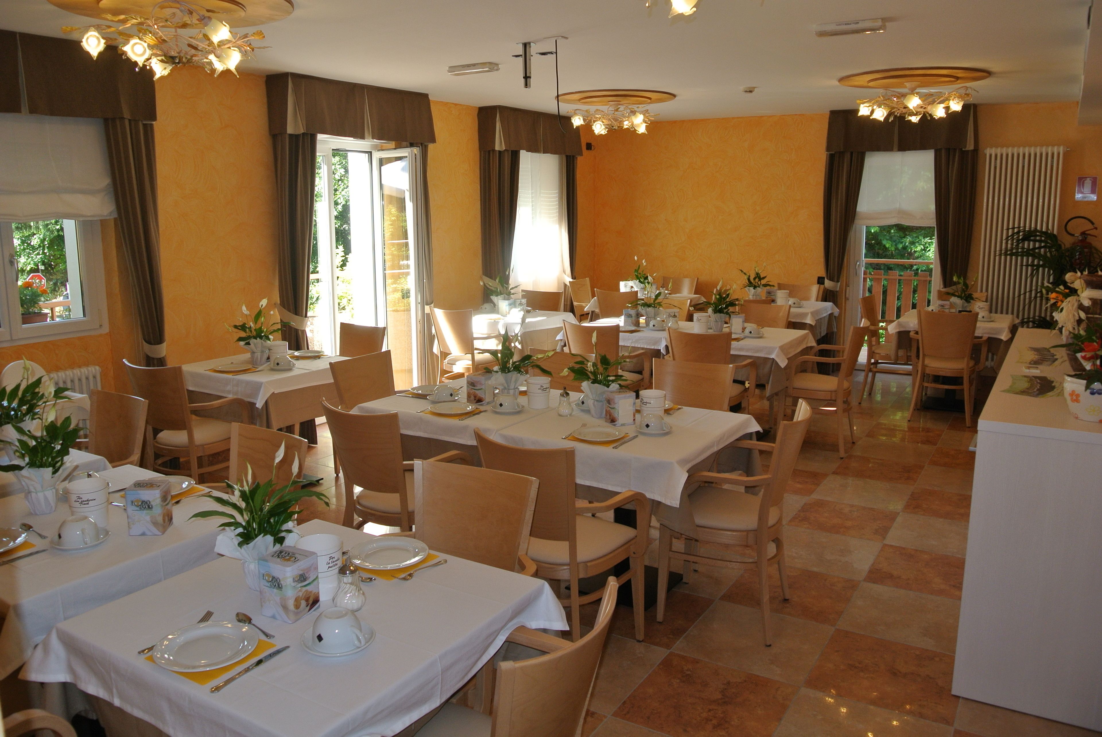 A dining area with multiple tables set for service, chairs, and decorative plants.
