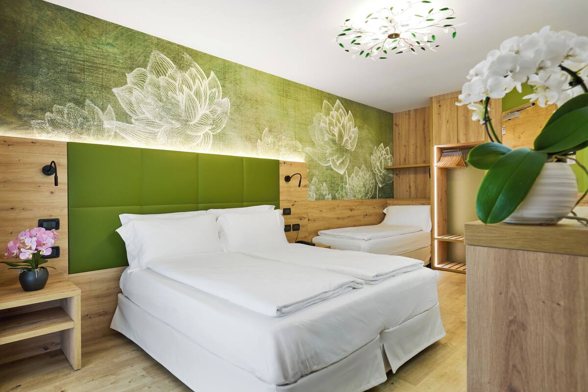 A modern hotel room with a large bed, a bedside table, a green accent wall, and a wooden headboard.