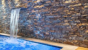 A stone wall with a waterfall feature and a blue pool.