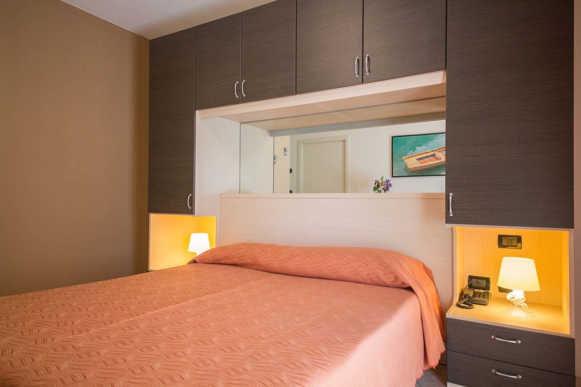 Habitación de hotel con cama, mesita de noche con lámpara, espejo e imagen en la pared.