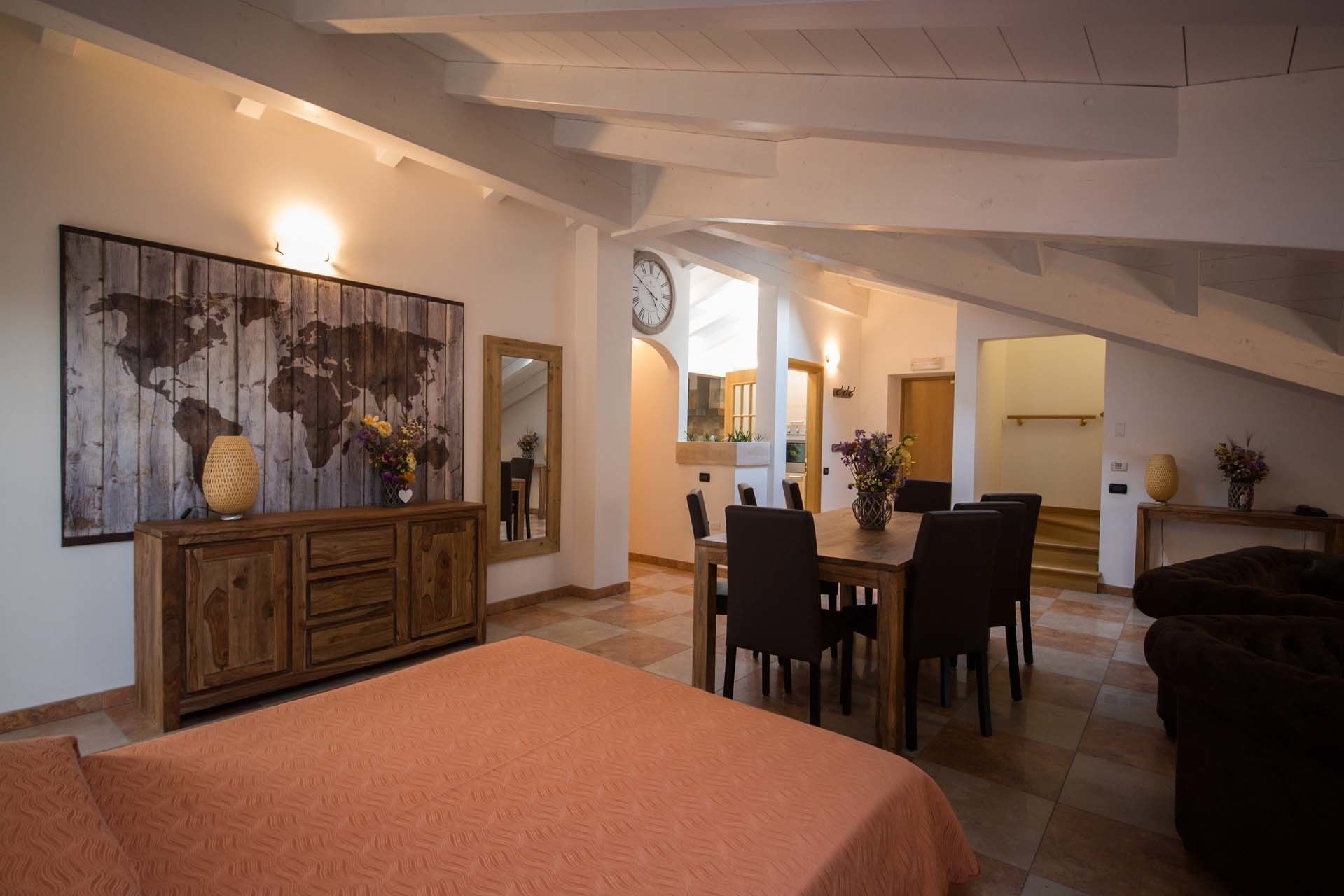 A spacious room with a large bed, a dining table with chairs, a wooden cabinet, and a world map artwork.