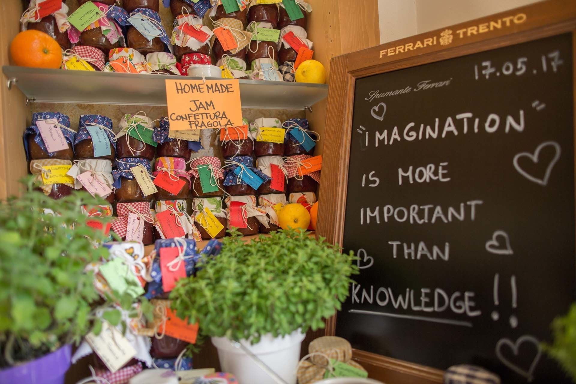 A display of homemade jam jars with colorful labels, a chalkboard with motivational writing, and a potted plant.