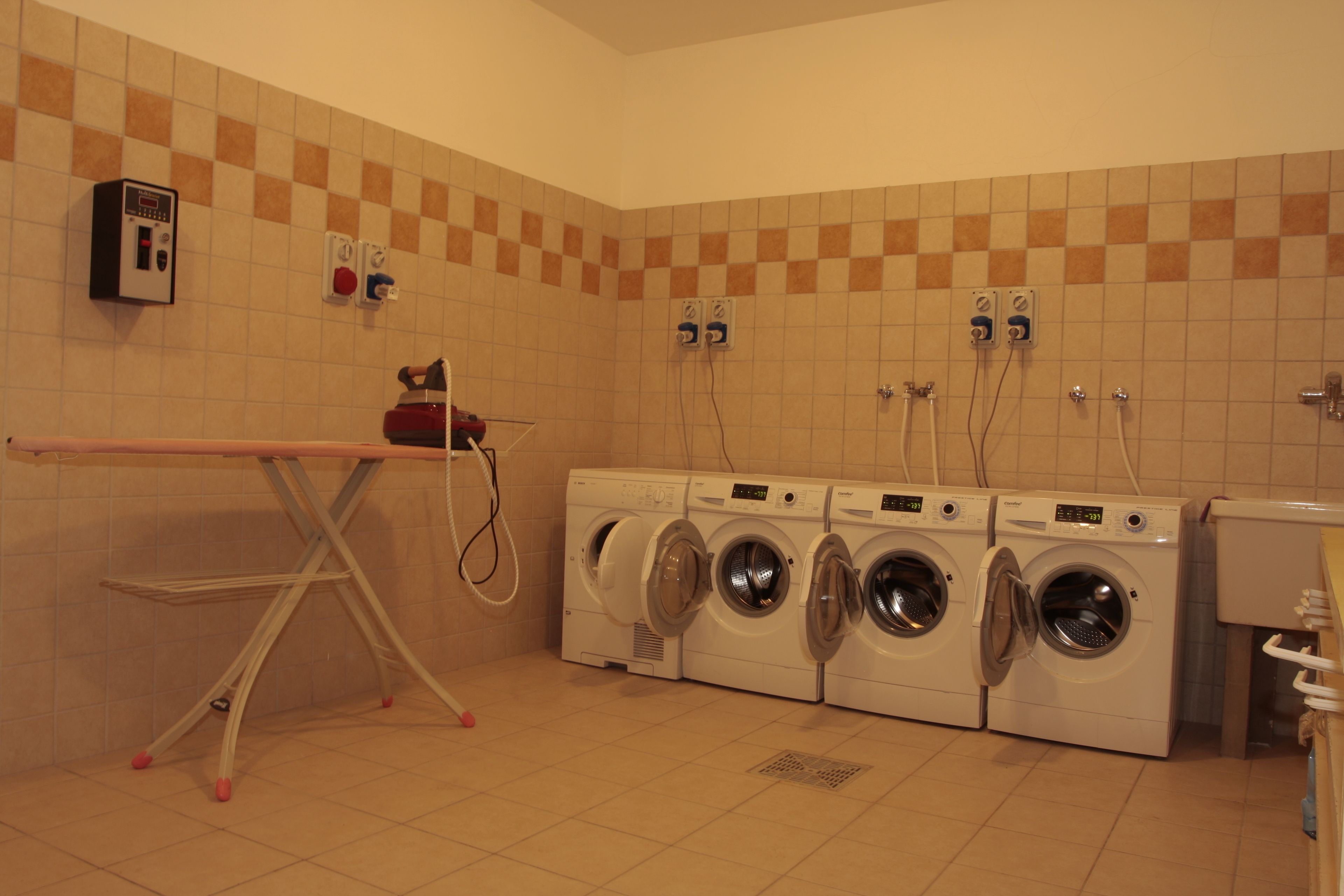 A laundry area with a drying rack, four washing machines, and a sink.