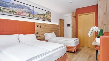 Habitació d'hotel amb dos llits, un capçal de llit de fusta, un quadre d'una ciutat, una porta de fusta i una taula amb una orquídia en test.