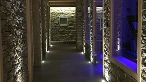 A corridor with stone walls and wooden beams, leading to a room with a stone wall and a window.
