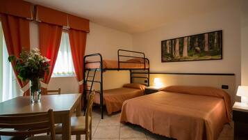 A dormitory room with bunk beds, a dining table with chairs, a vase with flowers, and a painting on the wall.
