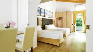 A hotel room with two beds, a desk, and a chair. There is a window with curtains, a painting on the wall, and a view of greenery outside.