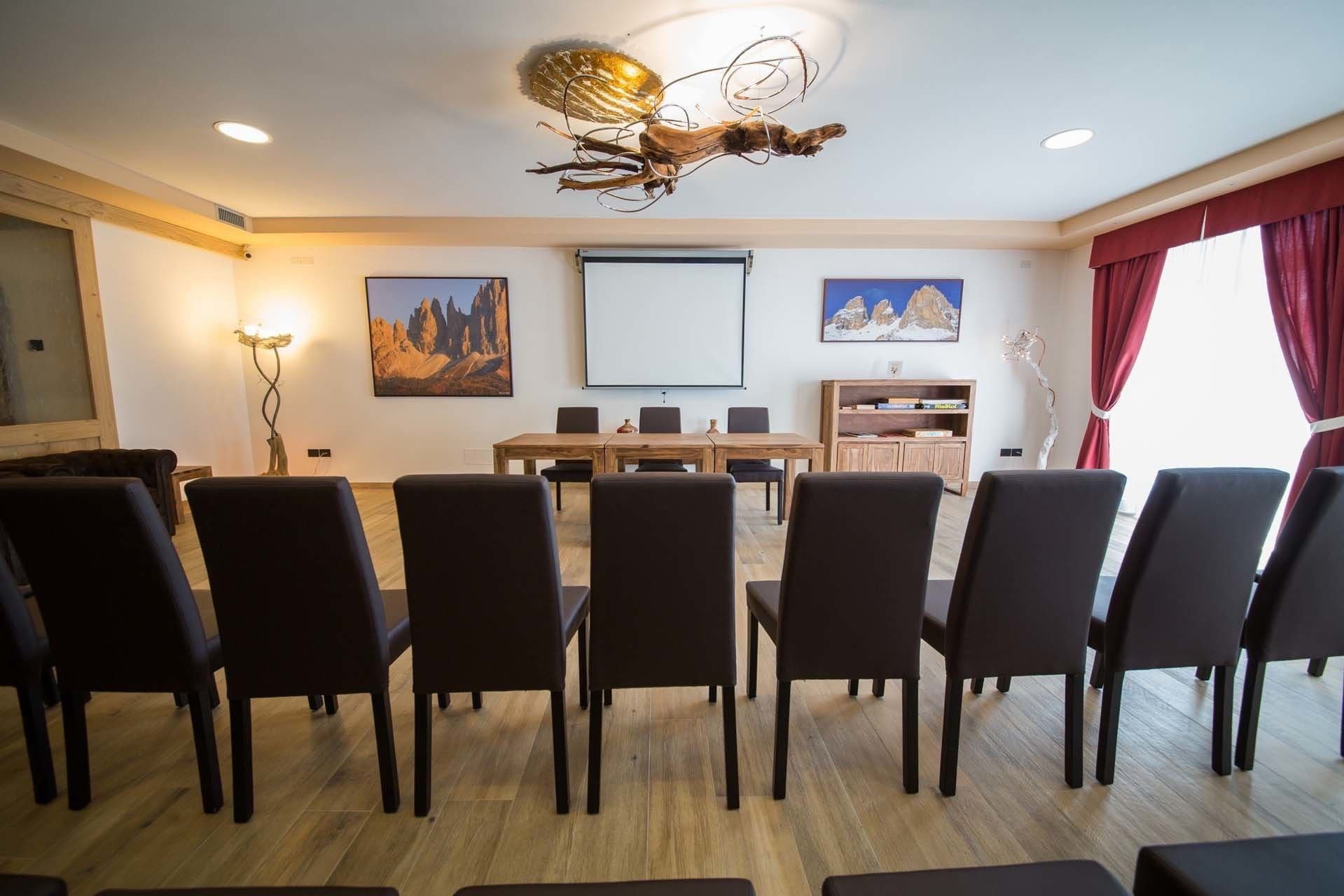 Uma sala de conferências com uma mesa de madeira, cadeiras pretas, uma tela de projetor e duas molduras na parede.
