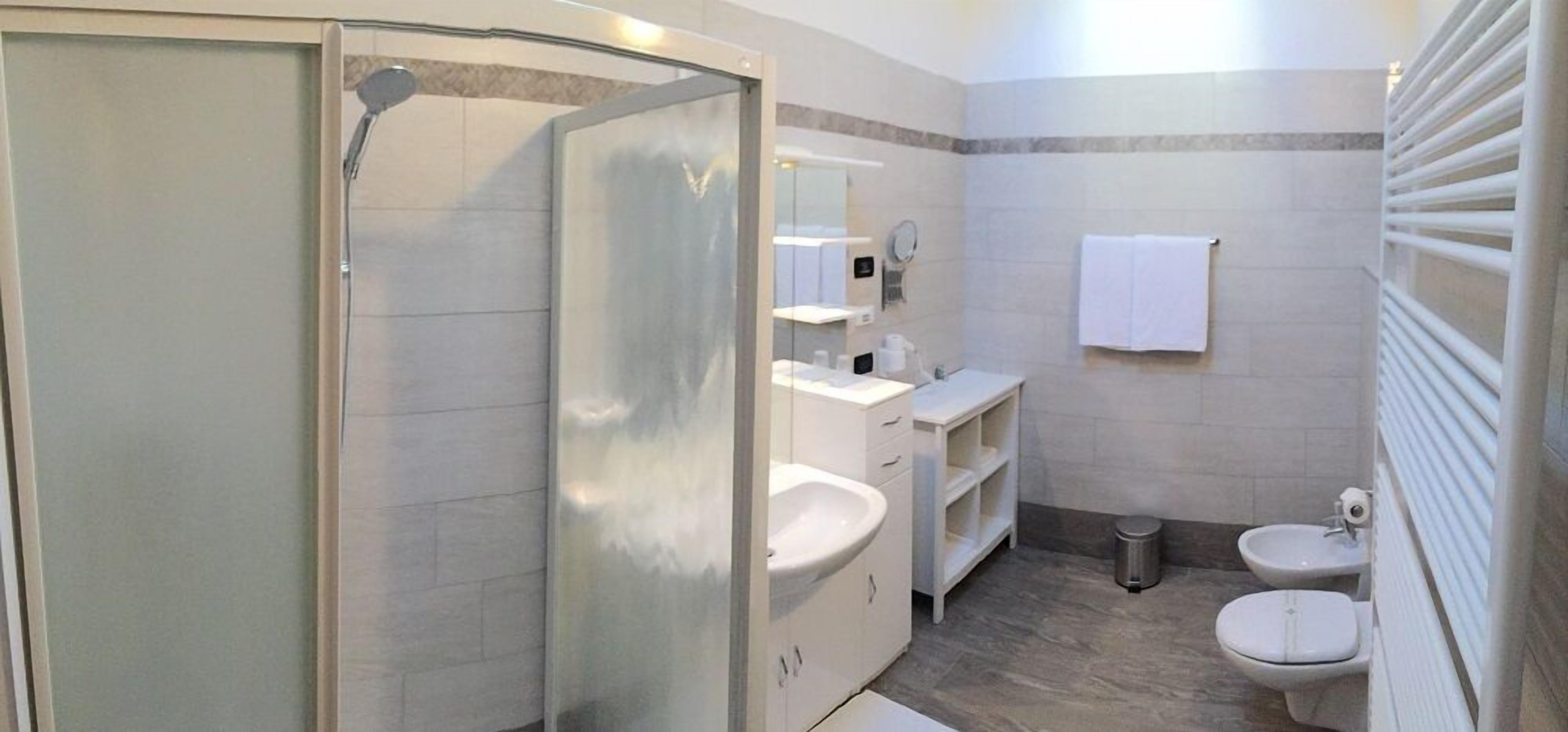Ein modernes Badezimmer mit einer Duschkabine aus Glas, einem Waschtisch mit Spiegel, zwei Waschbecken und einer Toilette.