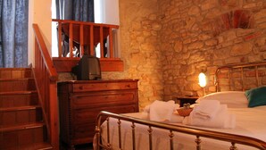 A bedroom with a stone wall, wooden staircase, a bed with white linens, and a nightstand with a lamp. - Hotel Bellavista (Bossolasco)