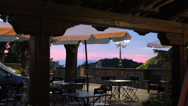 An outdoor patio with tables and chairs, a car parked nearby, and a sunset in the background. - Hotel Bellavista (Bossolasco)