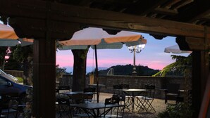 An outdoor patio with tables and chairs, a car parked nearby, and a sunset in the background. - Hotel Bellavista (Bossolasco)