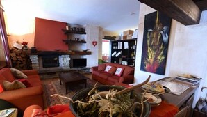 A cozy living room with a fireplace, red sofas, and a table with a bowl of herbs. - Hotel Bellavista (Bossolasco)