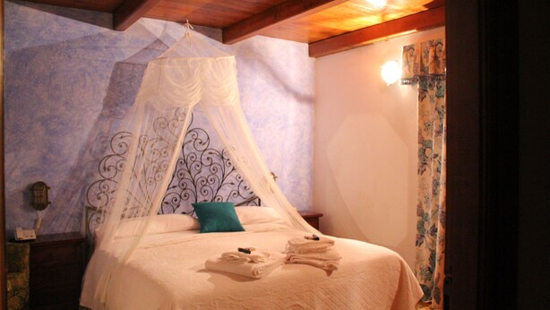 A bedroom with a canopy bed, a nightstand, and a wall-mounted lamp. - Hotel Bellavista (Bossolasco)