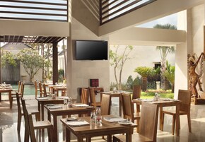 Restaurante com mesas e cadeiras de madeira, uma televisão de tela plana e vista para um jardim e piscina.