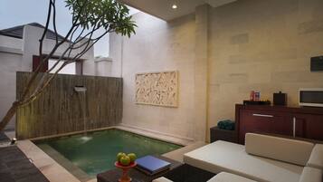 Un área de piscina moderna al aire libre con una silla de descanso, una mesita con un libro y manzanas, y un elemento decorativo en la pared.
