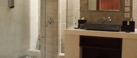 A modern bathroom with a glass-enclosed shower, a large mirror, and a beige vanity with a sink and countertop.