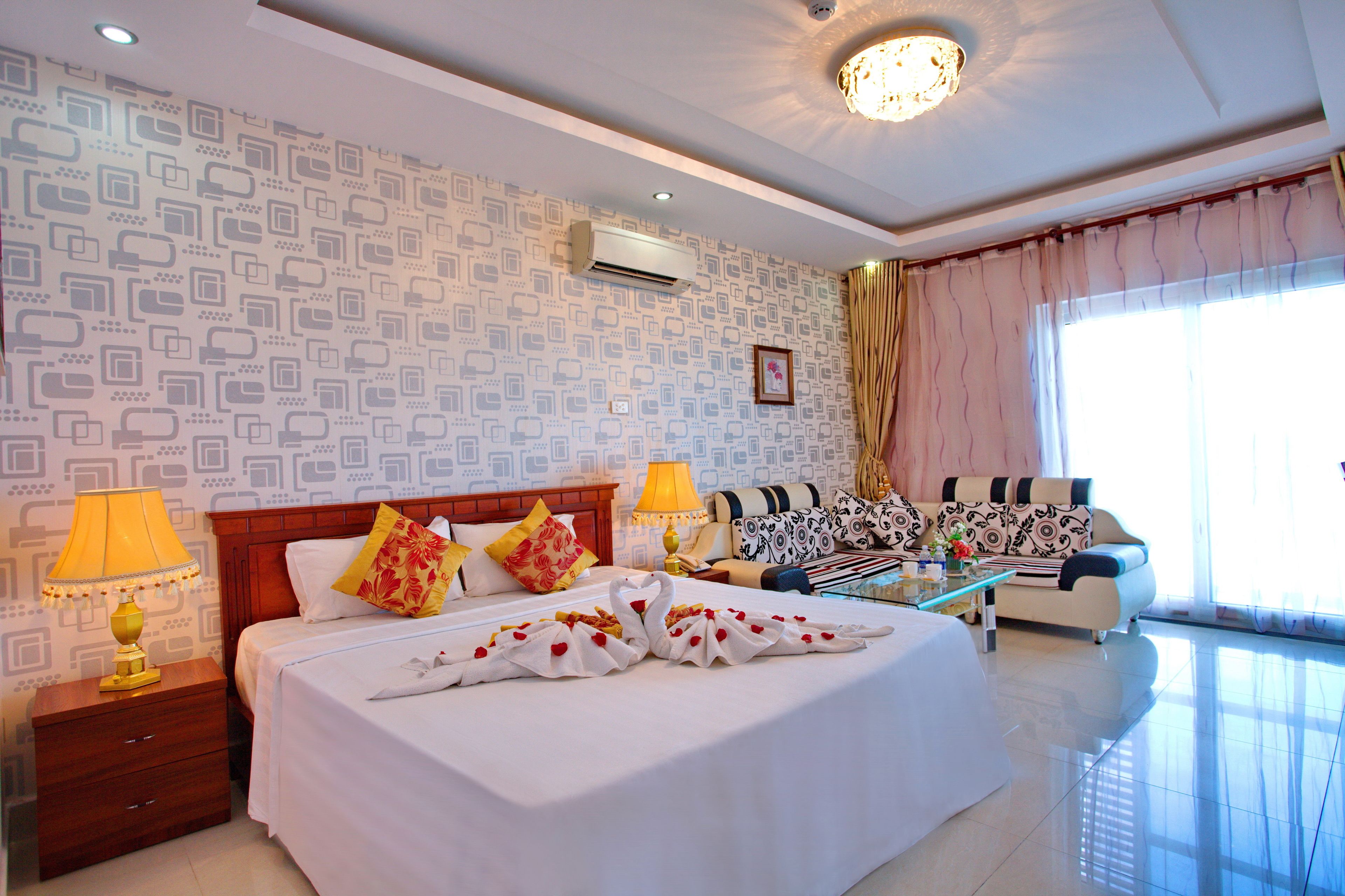 A hotel room with a large bed, two bedside tables, a sofa, and a window with curtains.