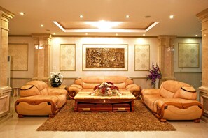 Uma sala de estar luxuosa com um sofá bege, uma mesa de centro de madeira com um arranjo floral e uma grande pintura abstrata na parede.